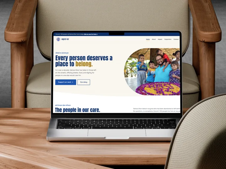 The Sahara Ghar home page on a laptop, open on a wooden table between two armchairs.